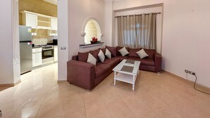 A living room with a brown sofa, a white coffee table, and a kitchen in the background. - Green Garden Resort (Hurghada)