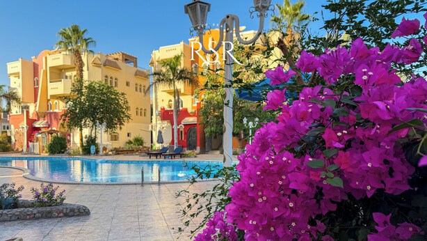 A hotel pool area with a clear view of the pool, lounge chairs, and a building with balconies. - Green Garden Resort (Hurghada)