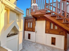 A wooden staircase leading to a white door with a small window, a tiled floor, and a stone structure to the left.