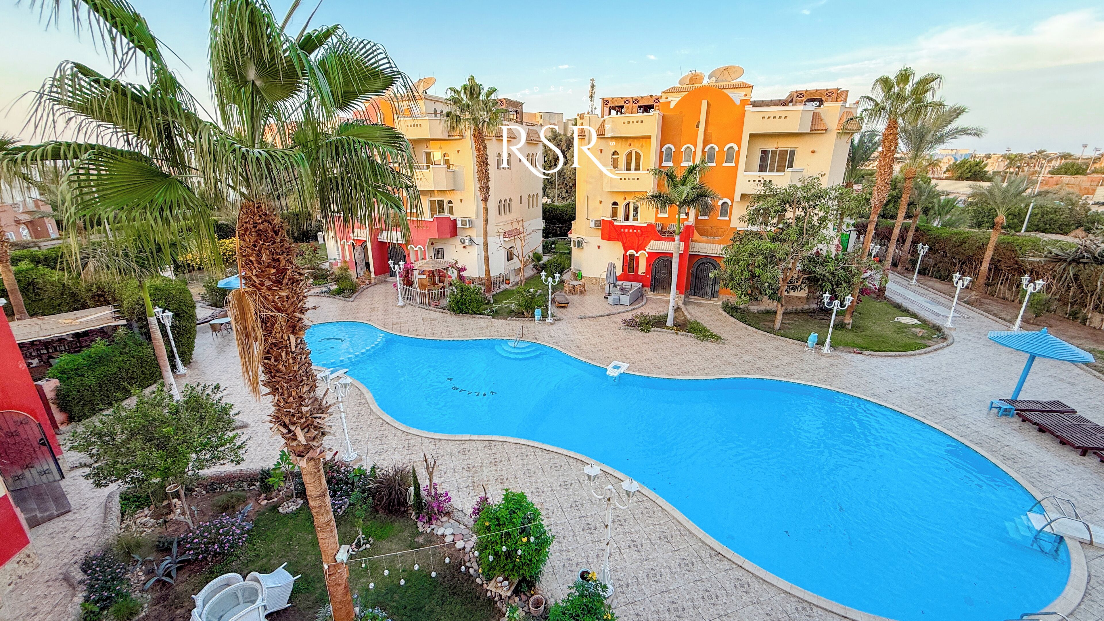 A swimming pool surrounded by palm trees and a building with balconies.