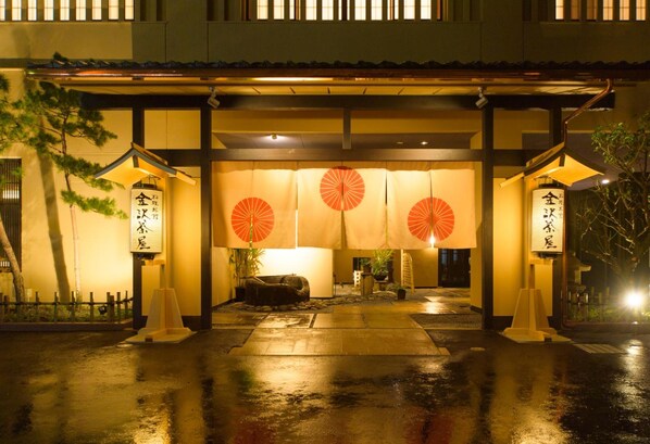 A traditional Japanese building entrance with a covered walkway, lanterns, and a stone lantern.