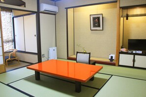 A traditional Japanese room with tatami flooring, a low orange table, a television, and a small refrigerator. - Kanazawa Chaya (Kanazawa)