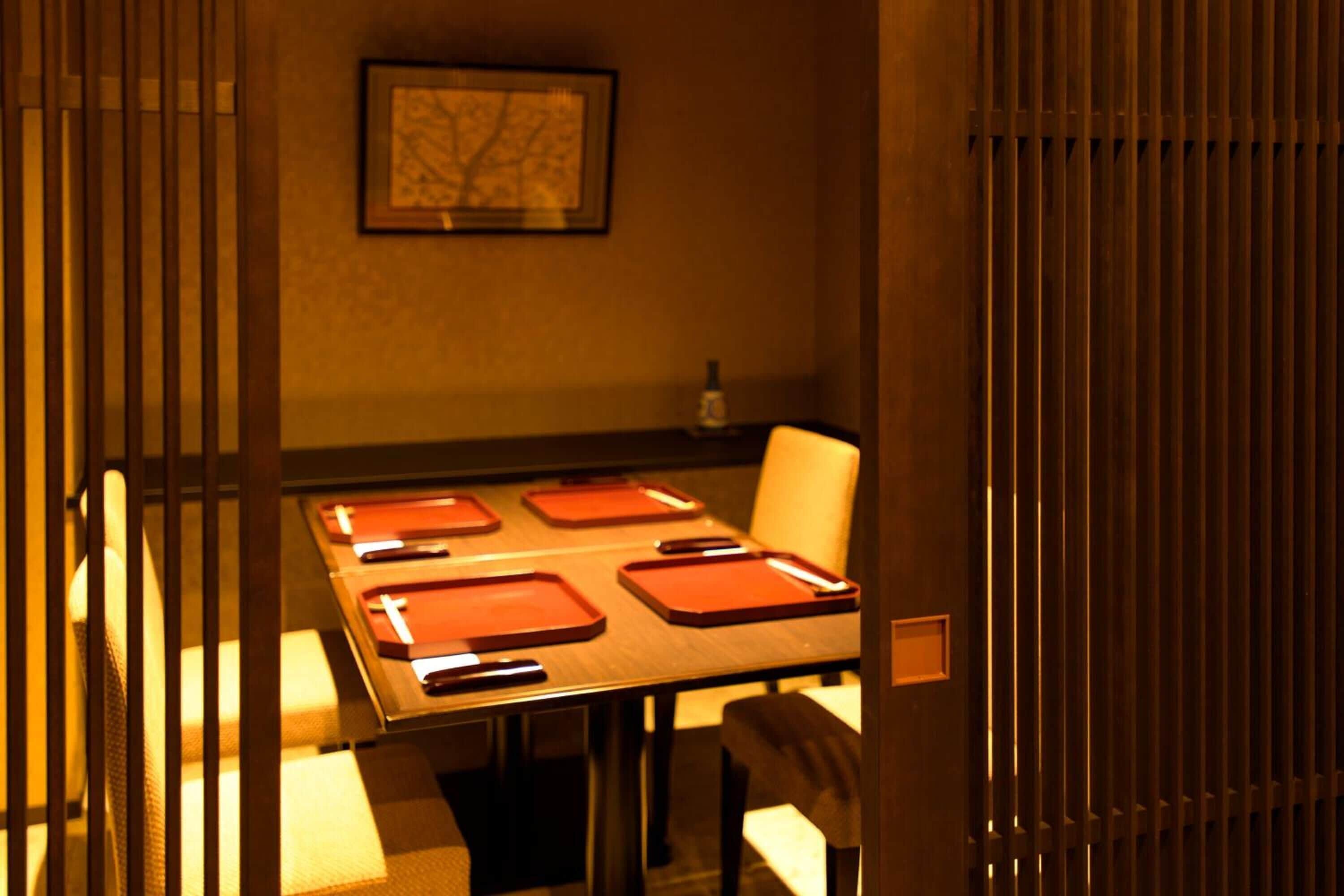Un coin repas avec une table dressée pour quatre personnes, un tableau encadré au mur et une bouteille posée sur la table.