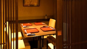 Uma sala de jantar com uma mesa posta para quatro pessoas, um quadro na parede e uma garrafa sobre a mesa.