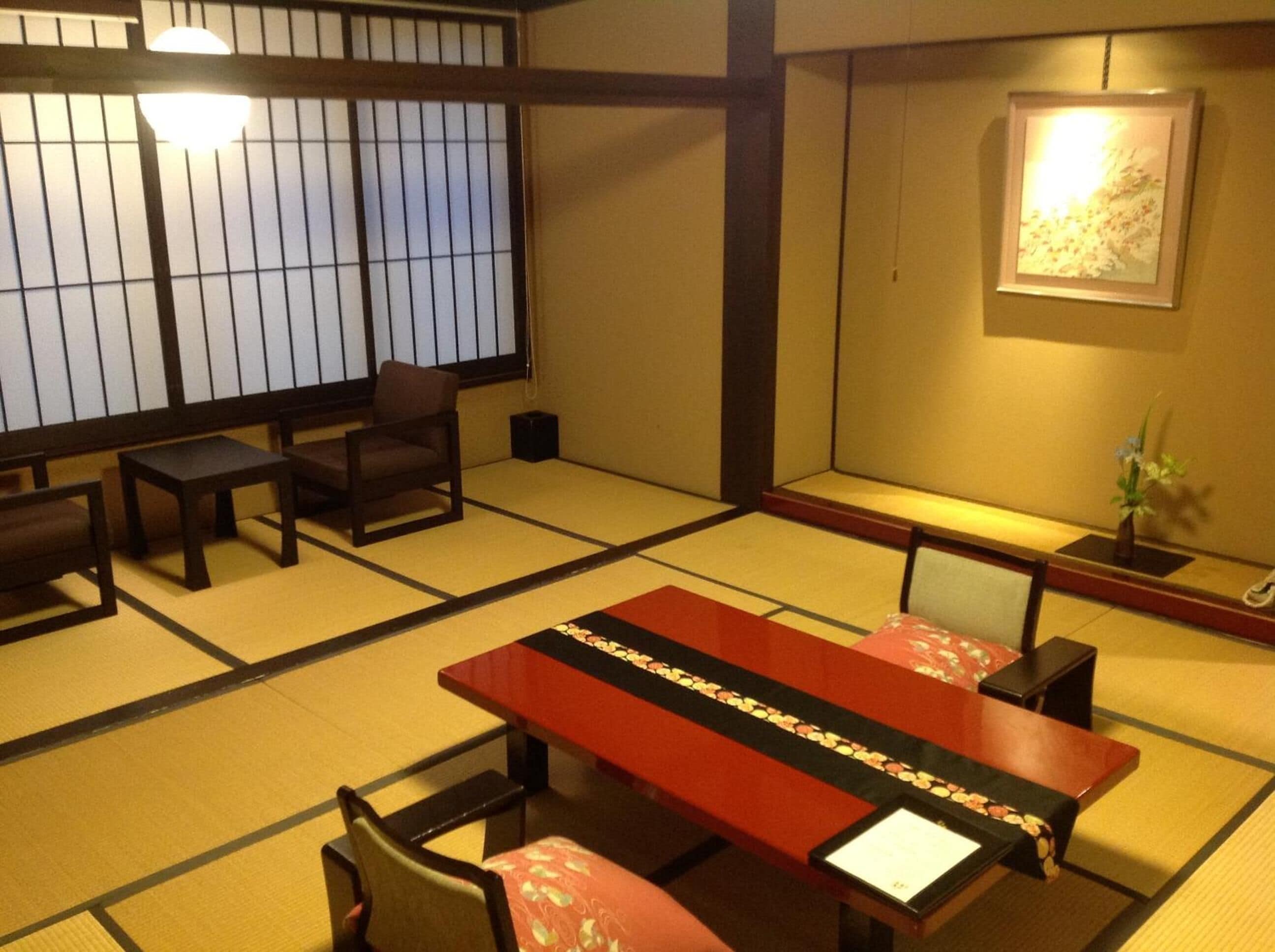 A traditional tatami mat room with a low table, chairs, and a sliding door.