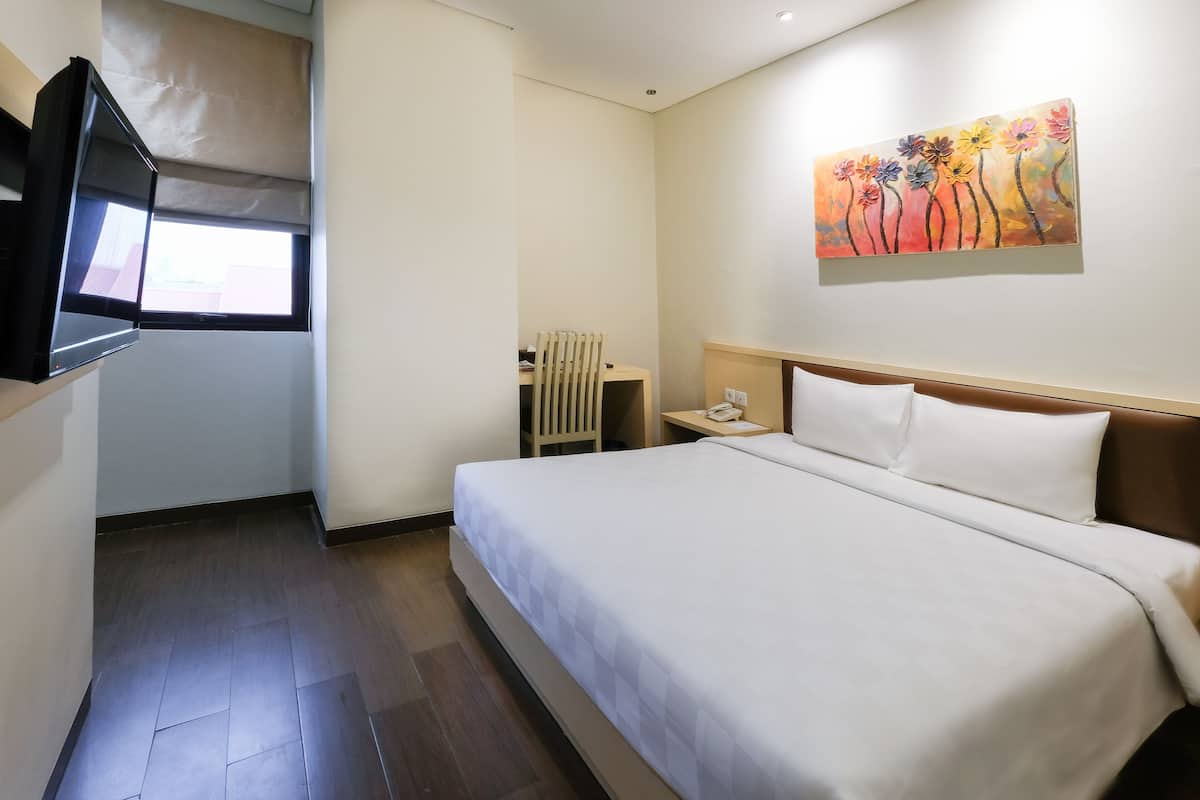A hotel room with a large bed, a flat-screen TV mounted on the wall, a bedside table with a lamp, and a painting on the wall.