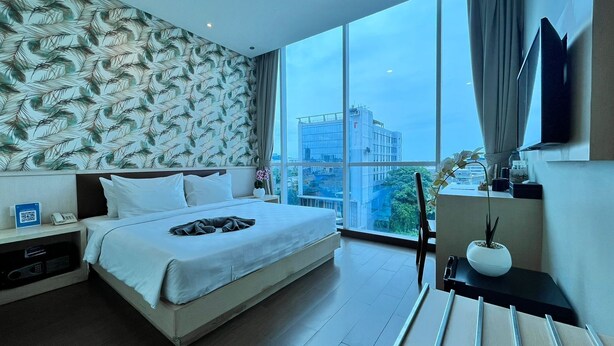 A modern hotel room with a large bed, a nightstand with a phone, a desk with a lamp, and a large window offering a city view. - Hotel 88 Mangga Besar 62 by WH (Jakarta)