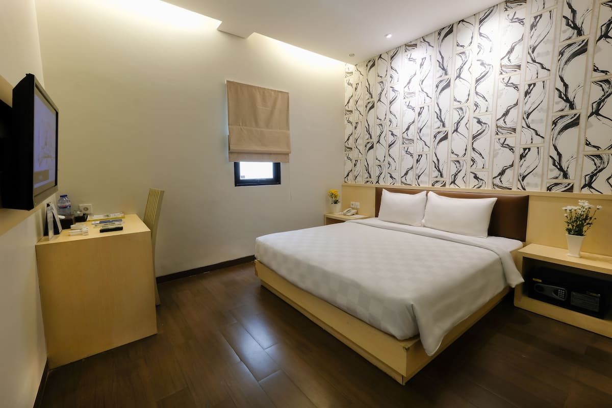 A modern hotel room with a large bed, a bedside table, a small window with a blind, and a wall with a black and white abstract pattern.