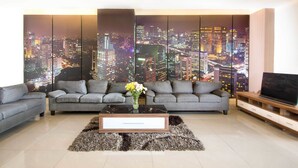 A modern living room with a cityscape view, grey sofas, a coffee table with a vase, and a TV on a wooden stand. - Hotel 88 Mangga Besar 62 by WH (Jakarta)