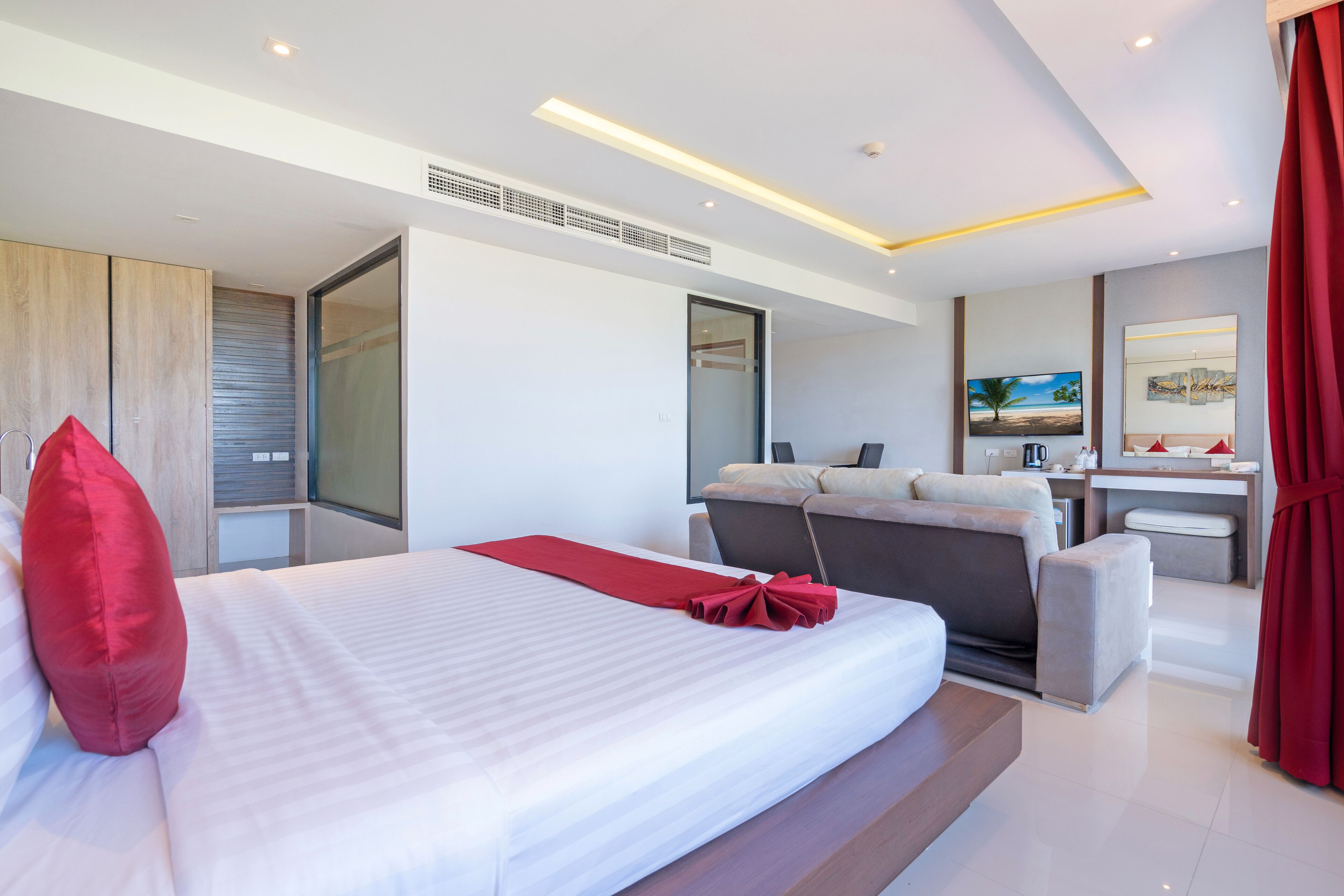 A modern hotel room with a large bed, a sofa, a desk, and a TV.