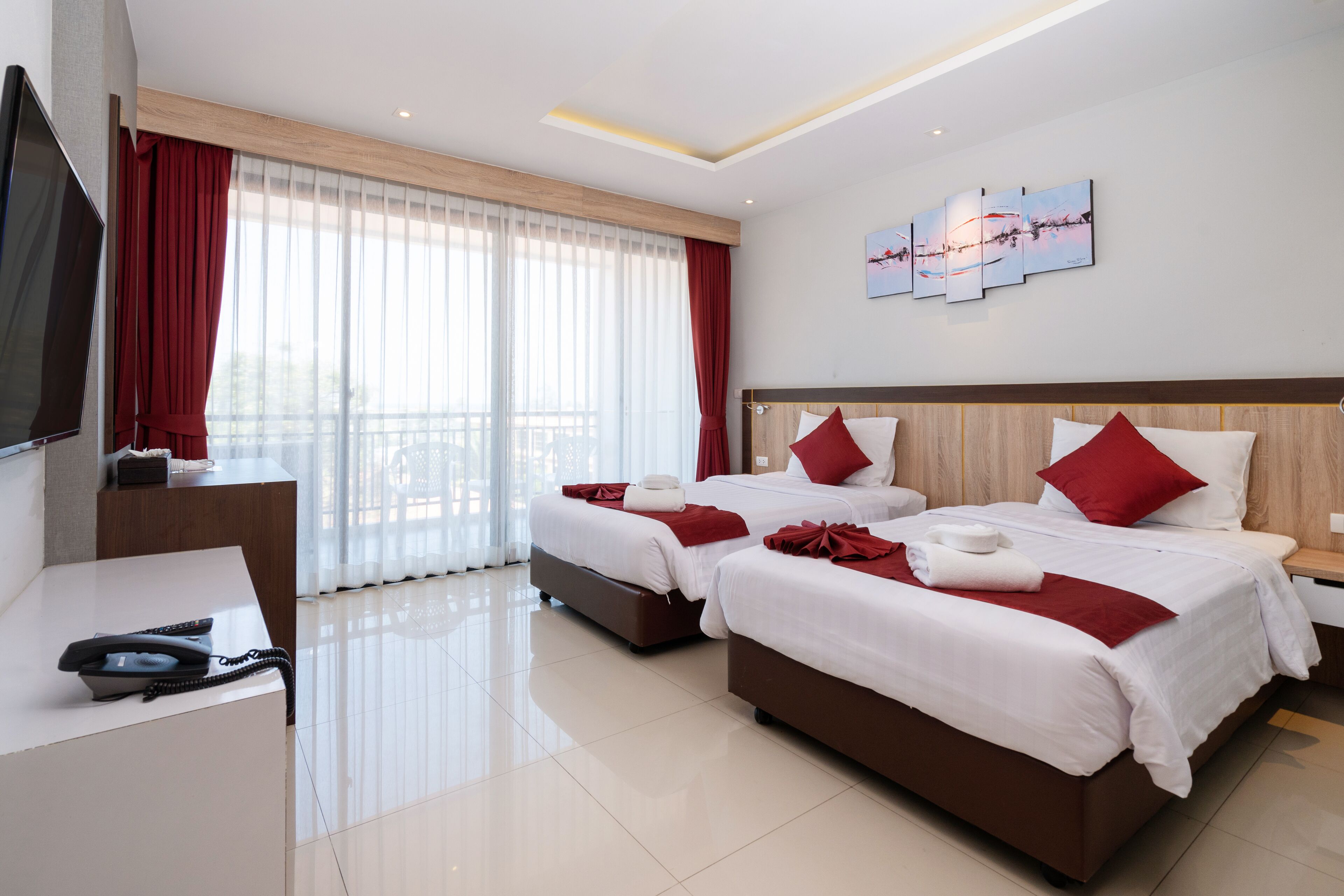 A hotel room with two beds, a TV, a desk, and a balcony with curtains.