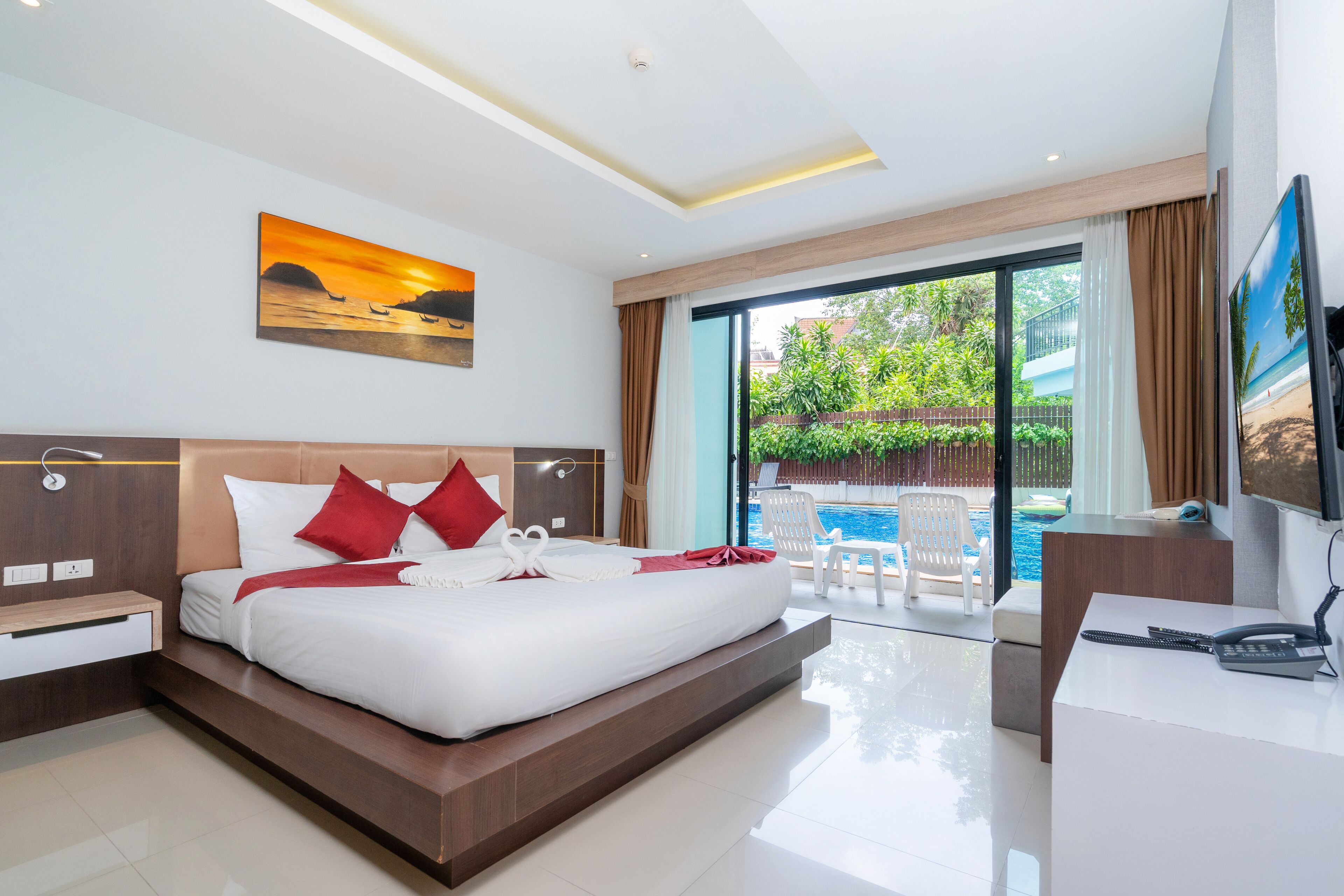 A modern hotel room with a large bed, a desk, a TV, and a view of a swimming pool and greenery.
