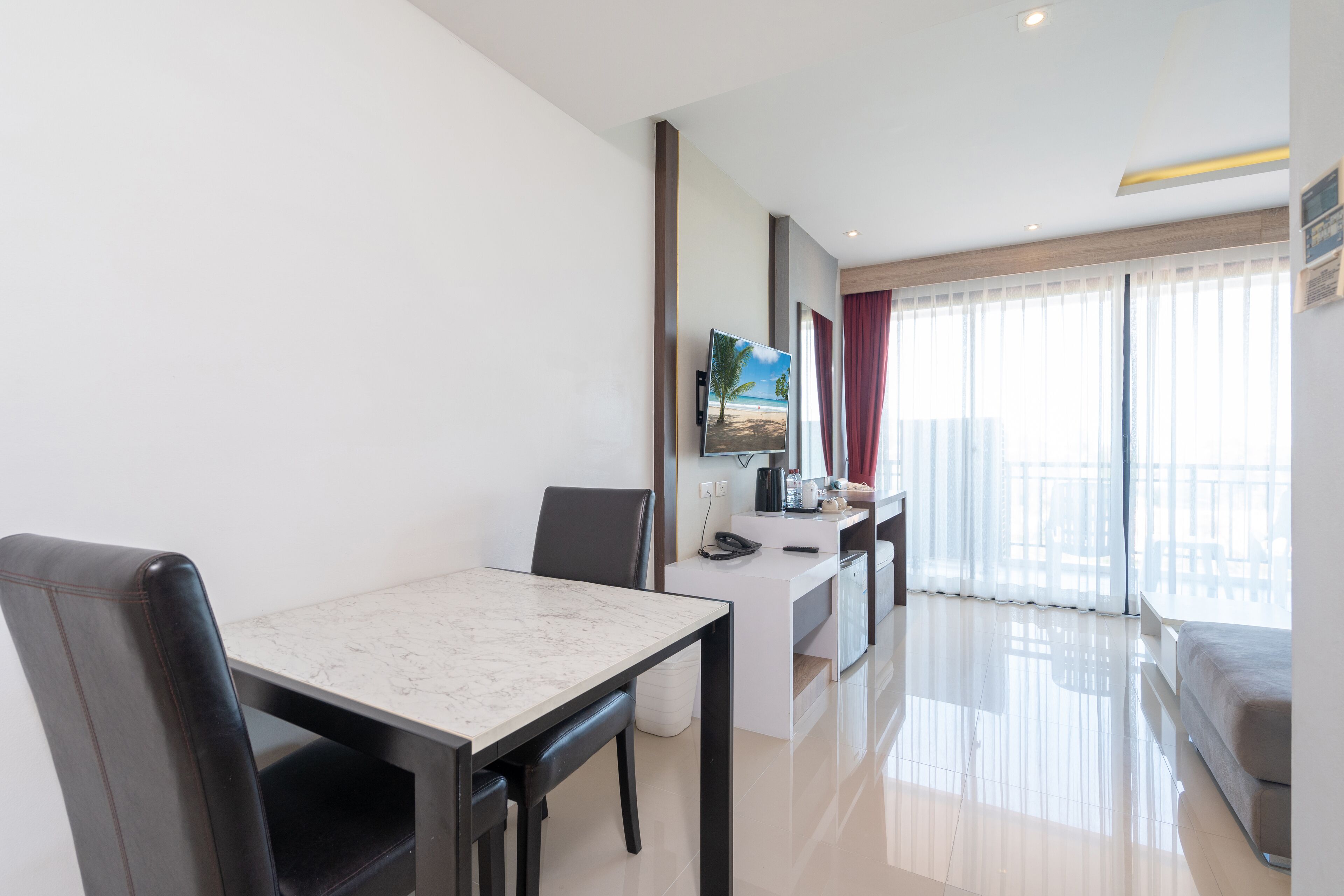 A modern hotel room with a dining area, a flat-screen TV, a balcony with a view, and a large window with curtains.