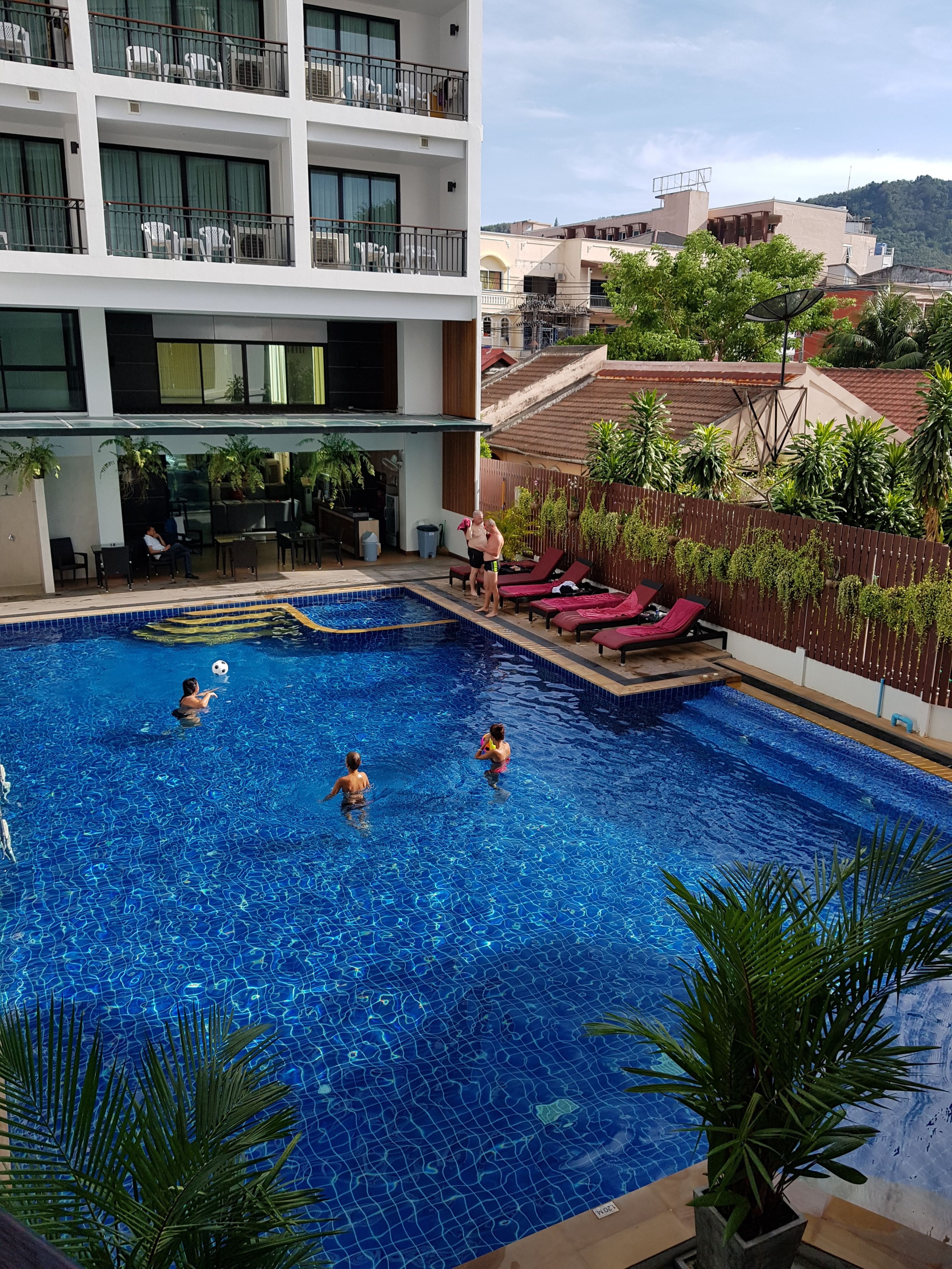 A swimming pool with multiple people, a covered seating area, and a view of surrounding buildings.