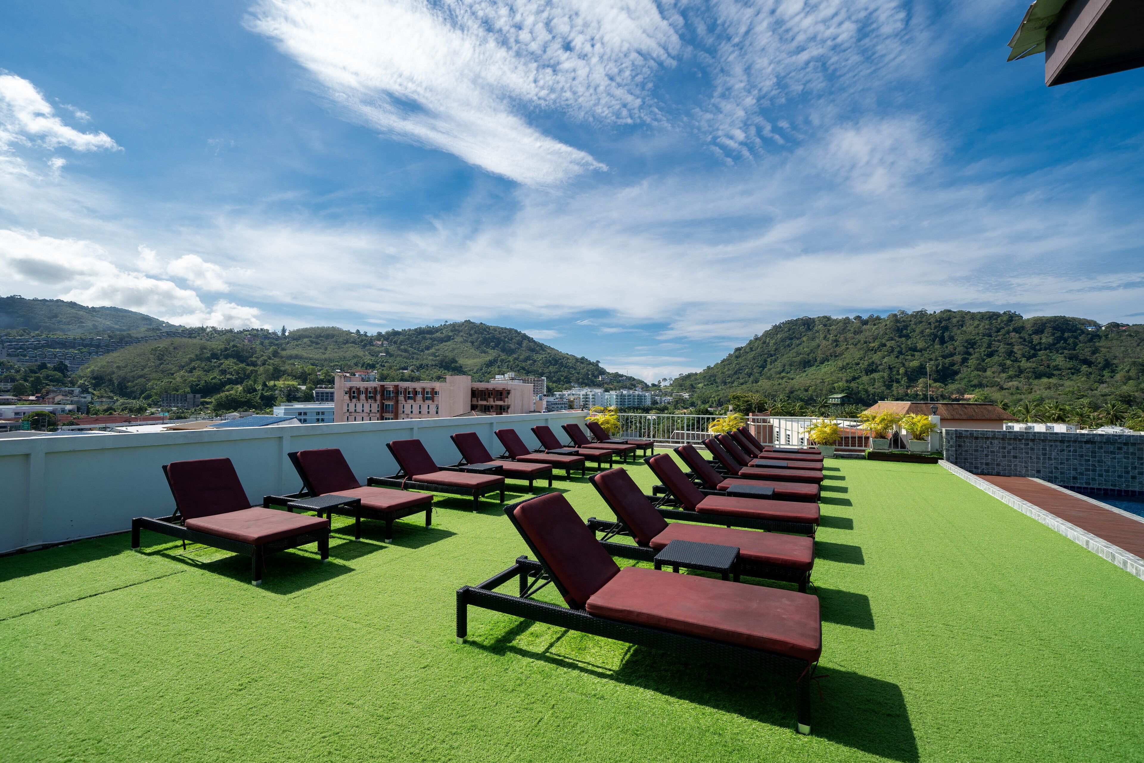A rooftop lounge with rows of sun loungers on artificial grass, overlooking a mountainous landscape.