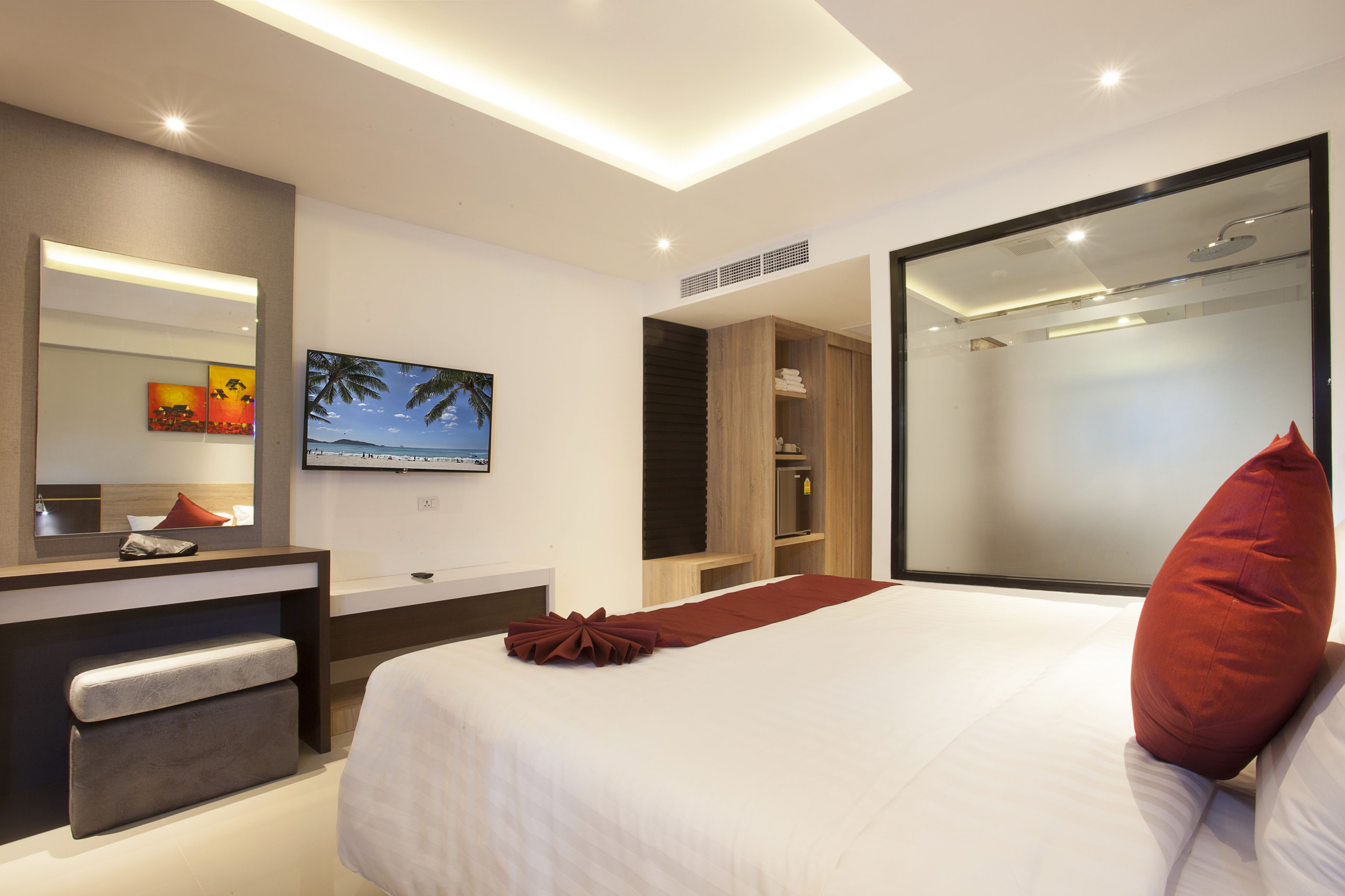 A modern hotel room with a large bed, a vanity with a mirror, a television, and a shower area.