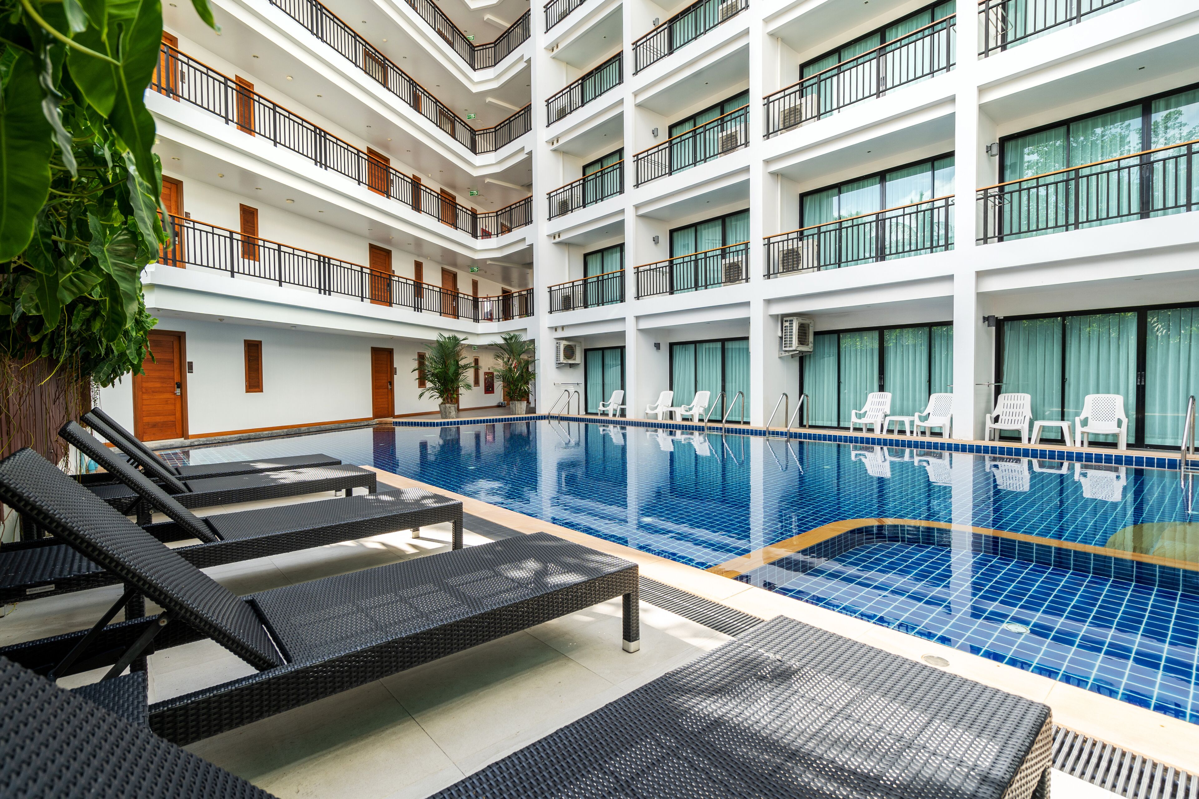 A multi-level hotel with a central swimming pool, lounge chairs, and a balcony with a view of the pool.