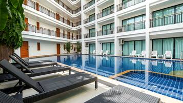 Un hotel de varios niveles con piscina central, sillas de descanso y un balcón con vistas a la piscina.
