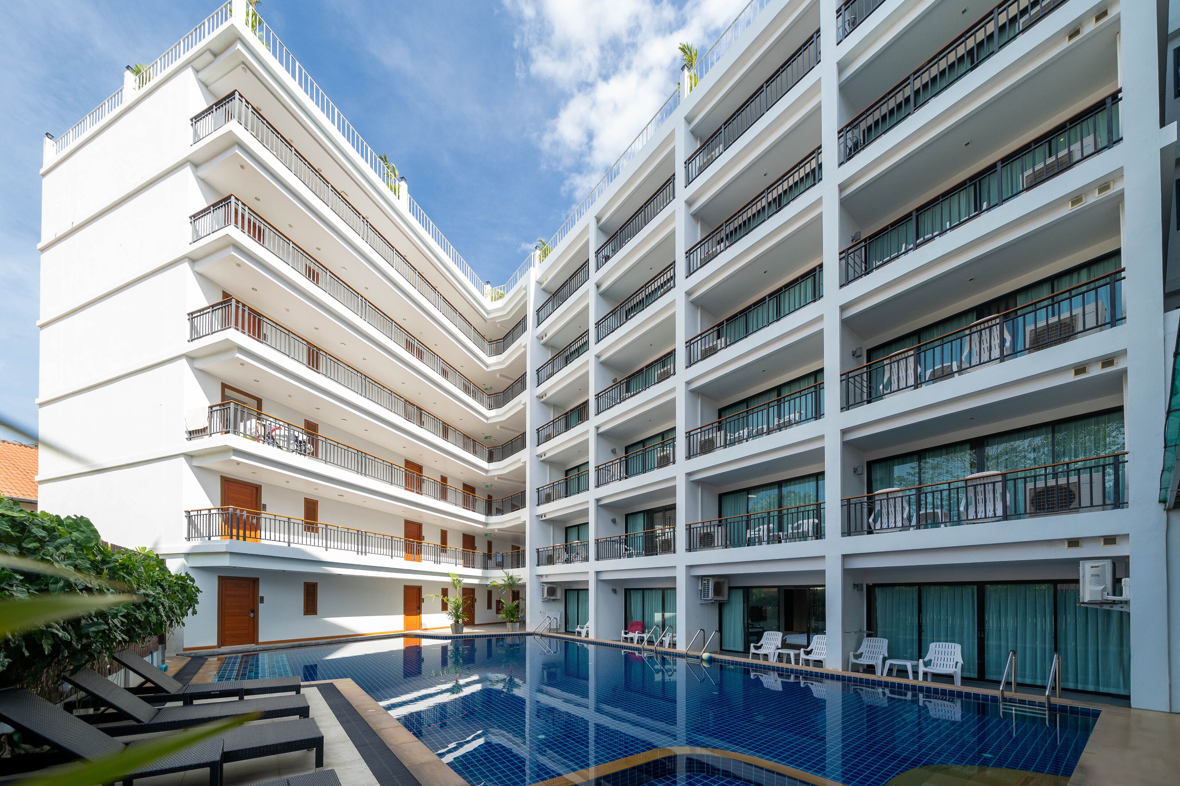 A multi-story hotel with a central swimming pool, balconies on each floor, and a clear sky.