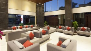 Un vestíbulo amplio con varios sofás grises y cojines rojos, ventanas grandes y un diseño de techo moderno.
