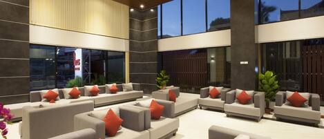 A spacious lobby with multiple grey sofas and red cushions, large windows, and a modern ceiling design.