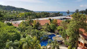 Un resort con una amplia piscina rodeada de exuberante vegetación, vista al mar y un paisaje montañoso al fondo.