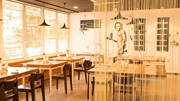 Un restaurante con mesas largas, lámparas colgantes y un amplio ventanal con vistas.