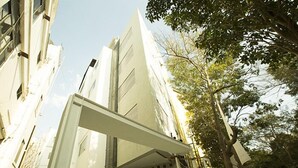 Un edificio moderno con fachada plana, ventanas grandes y un árbol en primer plano.