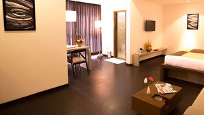 Habitación de hotel con cama, sofá, mesa de centro, televisor y escritorio con silla.