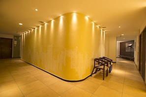 Un hall de hotel con un muro curvo, iluminación empotrada y una zona de estar con sillas de madera.