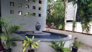 Un patio con una fuente, plantas en macetas y una estatua de Buda.