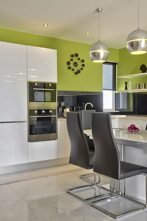 Une cuisine moderne avec des meubles blancs, des appareils en acier inoxydable et un coin repas doté de chaises noires.