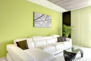 Un salon moderne avec un canapé blanc, une table basse en verre et un mur vert.