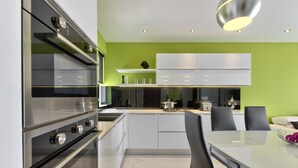 Una cocina moderna con un horno de acero inoxidable grande, armarios blancos y un comedor con mesa de vidrio y sillas negras.