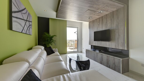Una sala de estar moderna con un sofá, una mesa de centro de vidrio y un televisor montado en una pared de madera.