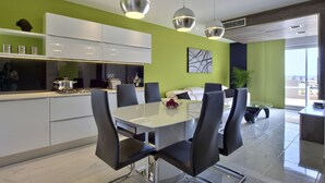 Una cocina moderna con armarios blancos, un área de comedor con mesa de vidrio y sillas negras, y una pared de acento verde.