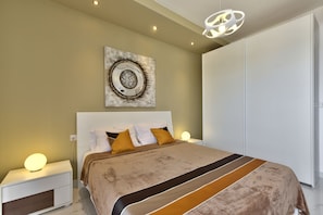 Une chambre moderne avec un grand lit, une table de chevet avec une lampe, une œuvre d’art accrochée au mur et une armoire.