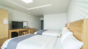 Habitación de hotel con dos camas, un escritorio con televisor y una kitchenette pequeña.