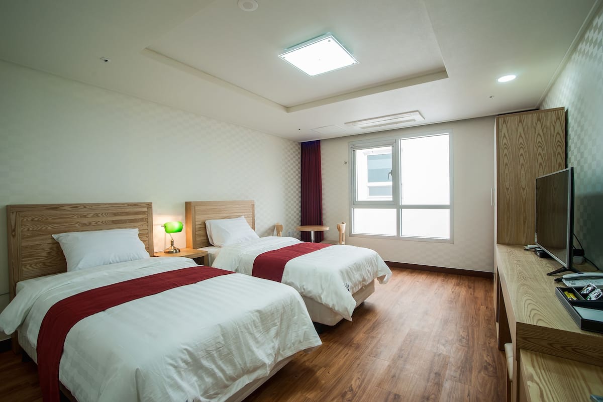 Ein Hotelzimmer mit zwei Betten, einem Schreibtisch, einem Fernseher und einem Fenster.