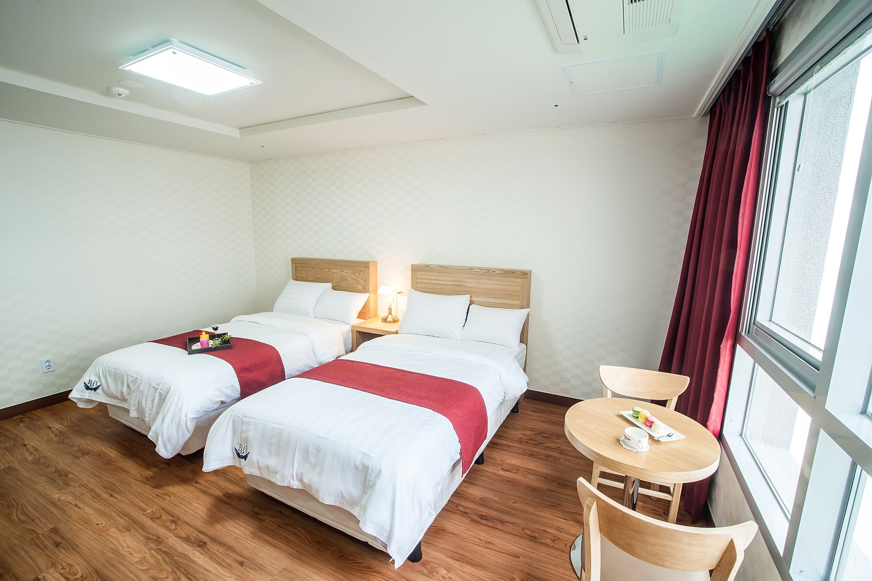 Habitación de hotel con dos camas, una mesita pequeña con una silla y una ventana con cortinas.