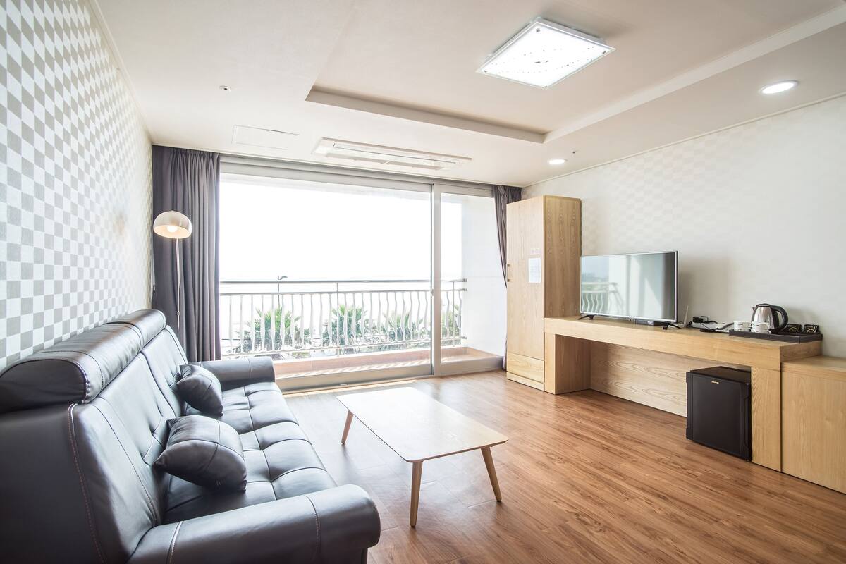 Ein modernes Wohnzimmer mit einer Ledersofa, einem Holztisch, einem Flachbildfernseher und einer Küchenzeile mit Kühlschrank und Kaffeemaschine.