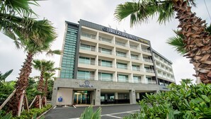 Un hotel de varios pisos con diseño moderno, que cuenta con balcones en cada planta y un área de estacionamiento al frente.