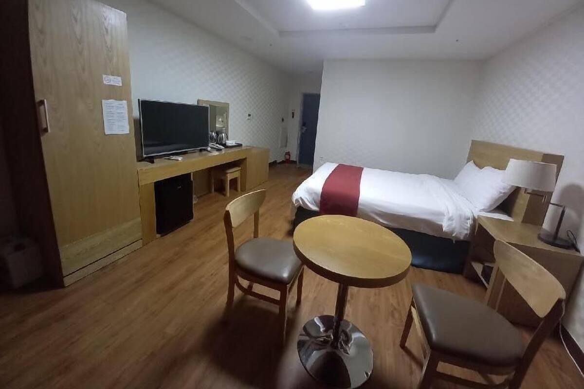 Ein Hotelzimmer mit einem Bett, einem Schreibtisch mit Computer, einem Stuhl, einem kleinen Tisch und einem Fernseher.
