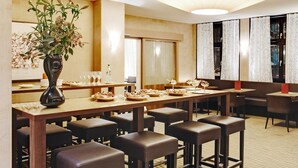 A restaurant with a long wooden table, multiple bar stools, and a large vase of flowers. - Congress Apartments by Hotel du Commerce (Basel)