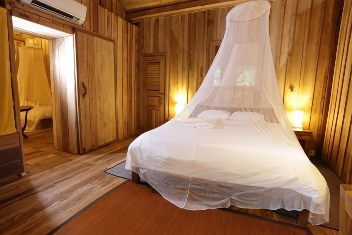 A wooden room with a bed, a door, and a wall-mounted air conditioner.