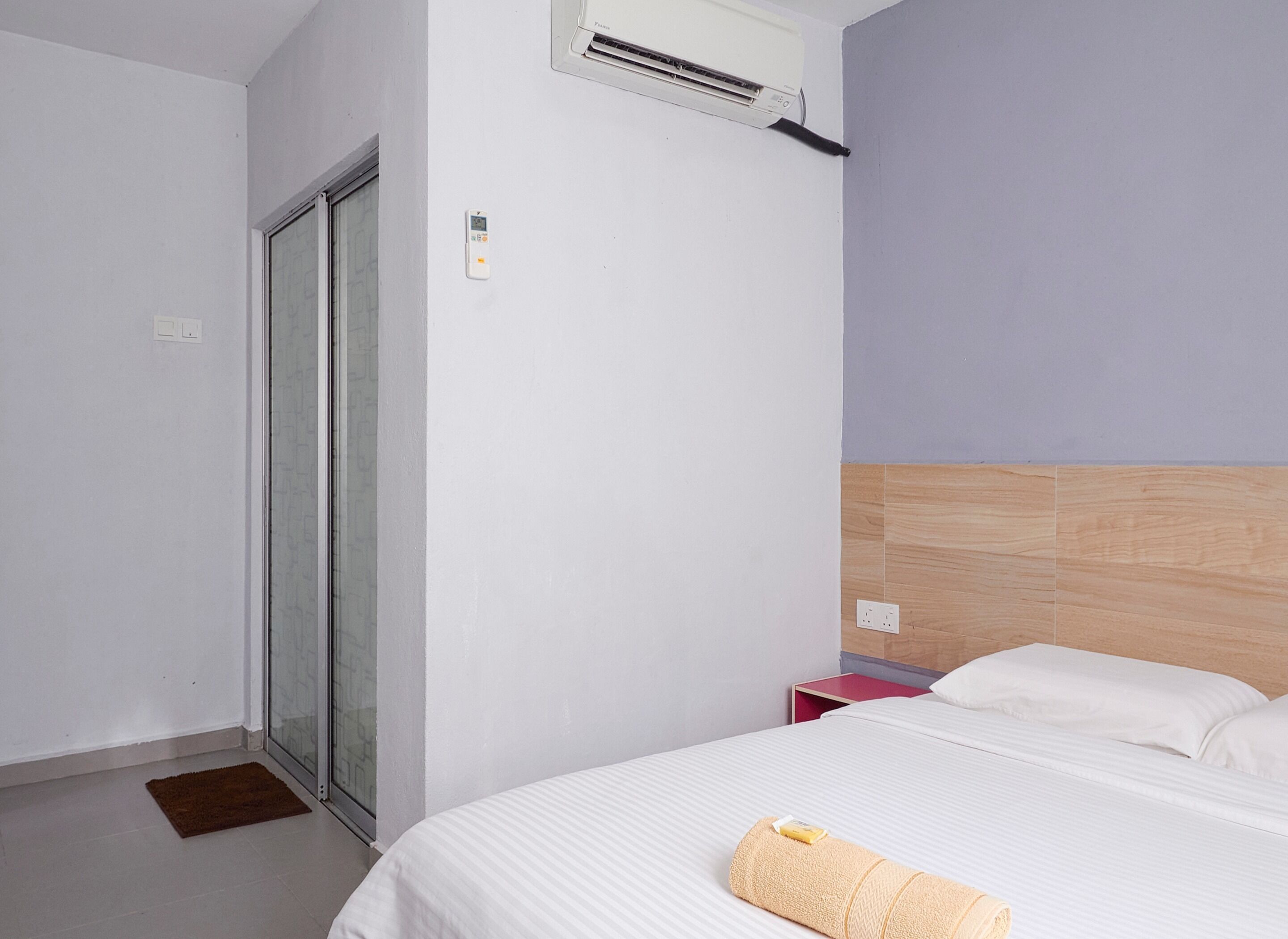 A hotel room with a bed, a sliding glass door, a thermostat, and a nightstand.