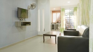 A living room with a flat-screen TV mounted on the wall, a wooden coffee table, a black sofa, and a window with green curtains. - Corrie Chalet Pantai Cenang Langkawi (Langkawi)