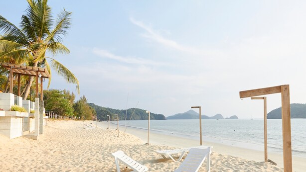 A beach with white lounge chairs and a wooden structure. - Corrie Chalet Pantai Cenang Langkawi (Langkawi)