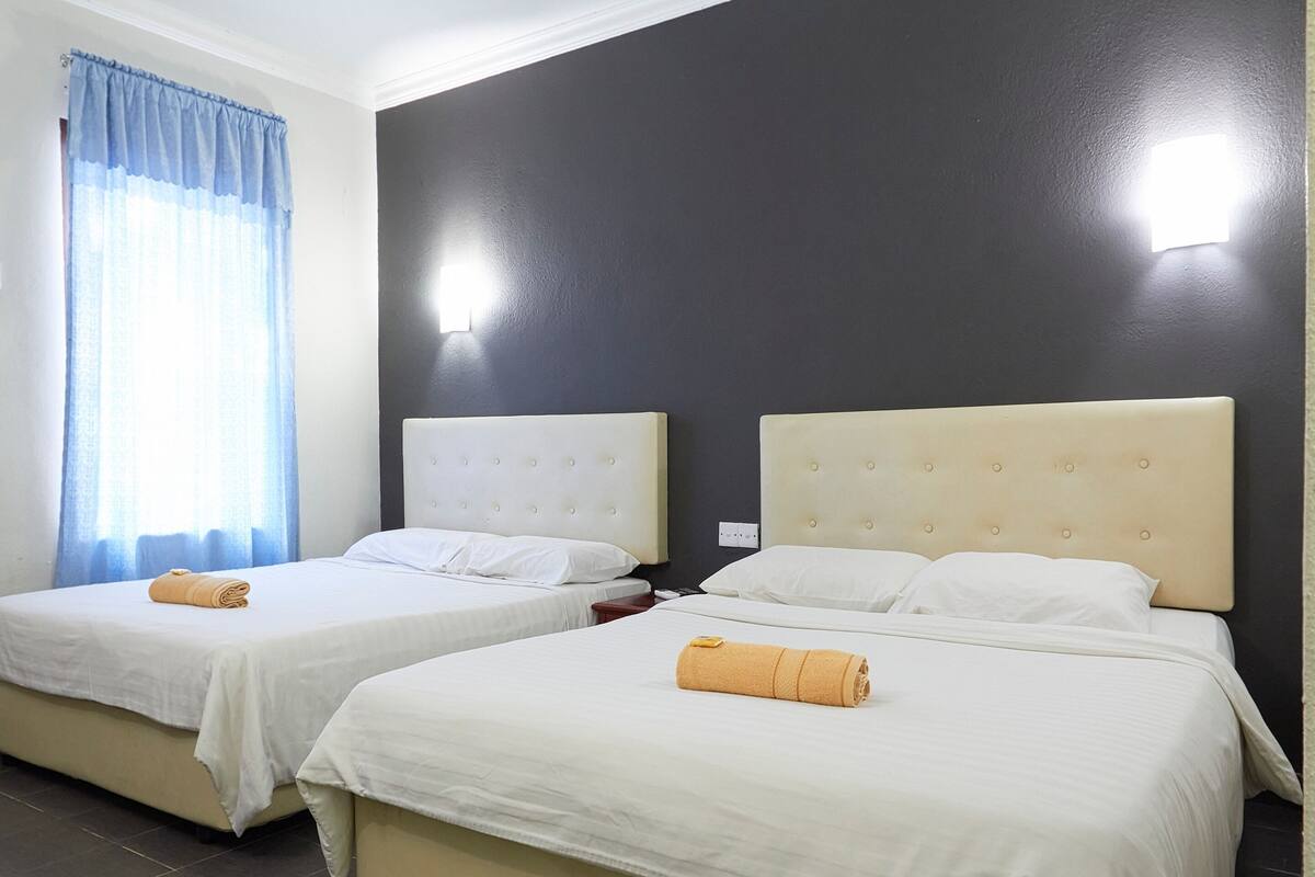 A hotel room with two beds, each with a headboard and a rolled towel on the bed.