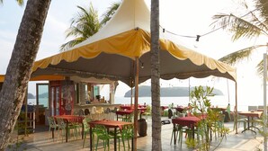 An outdoor seating area with tables and chairs under a canopy, overlooking a body of water. - Corrie Chalet Pantai Cenang Langkawi (Langkawi)